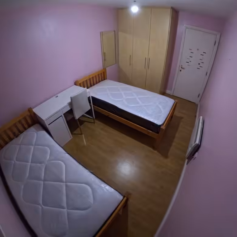 Bedroom with two beds, desk, wardrobe, and pink walls.