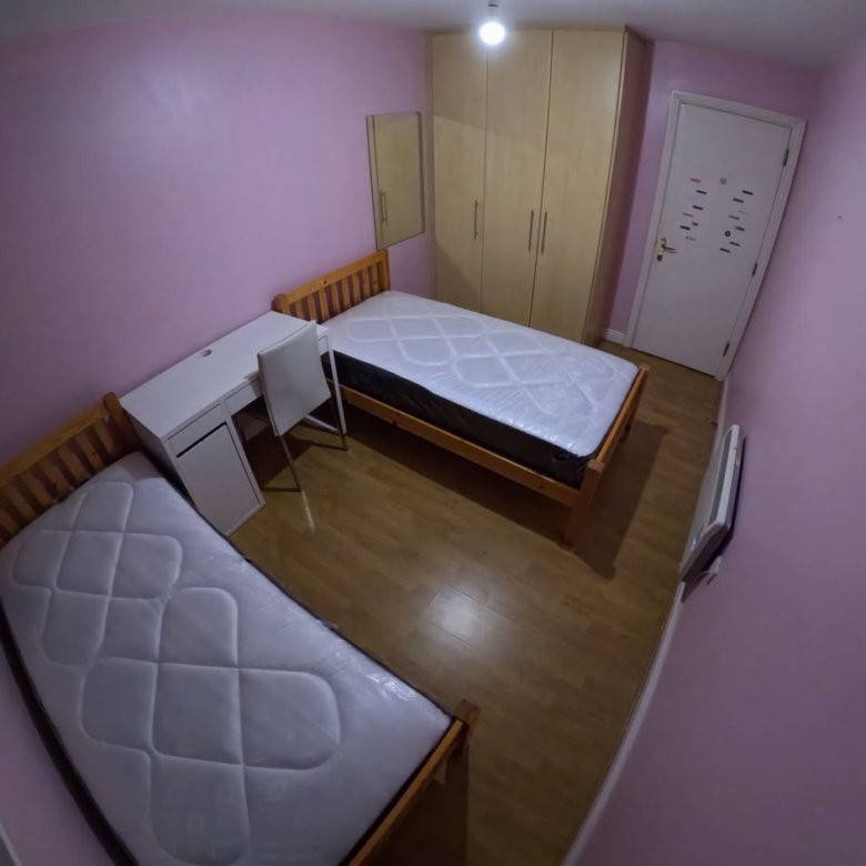 Bedroom with two beds, desk, wardrobe, and pink walls.