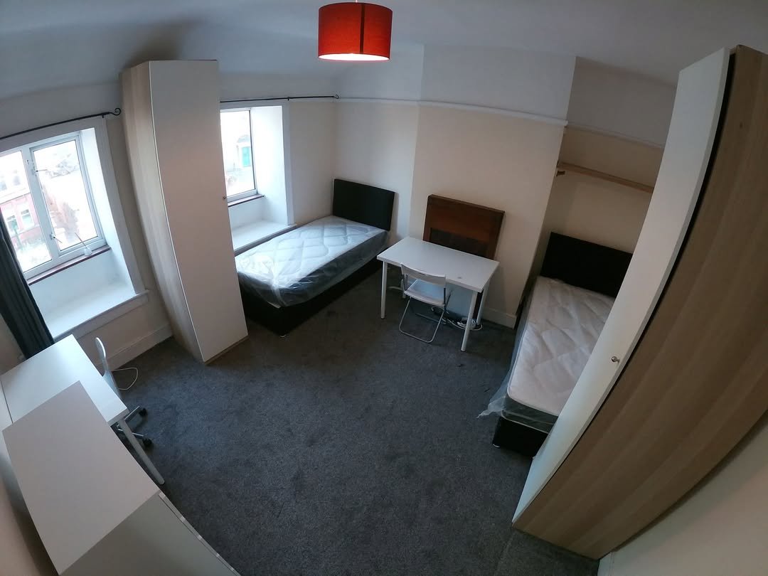Bedroom with two beds, desks, wardrobes, and a gray carpet. Bright room with natural light from windows.