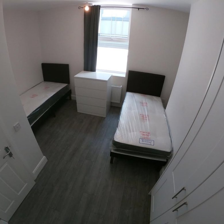 Bedroom with two beds, dresser, and grey wood floors.