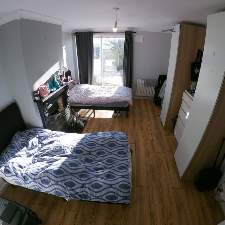 Bedroom with two beds, wardrobe, and wooden floor. Bright sunlight.
