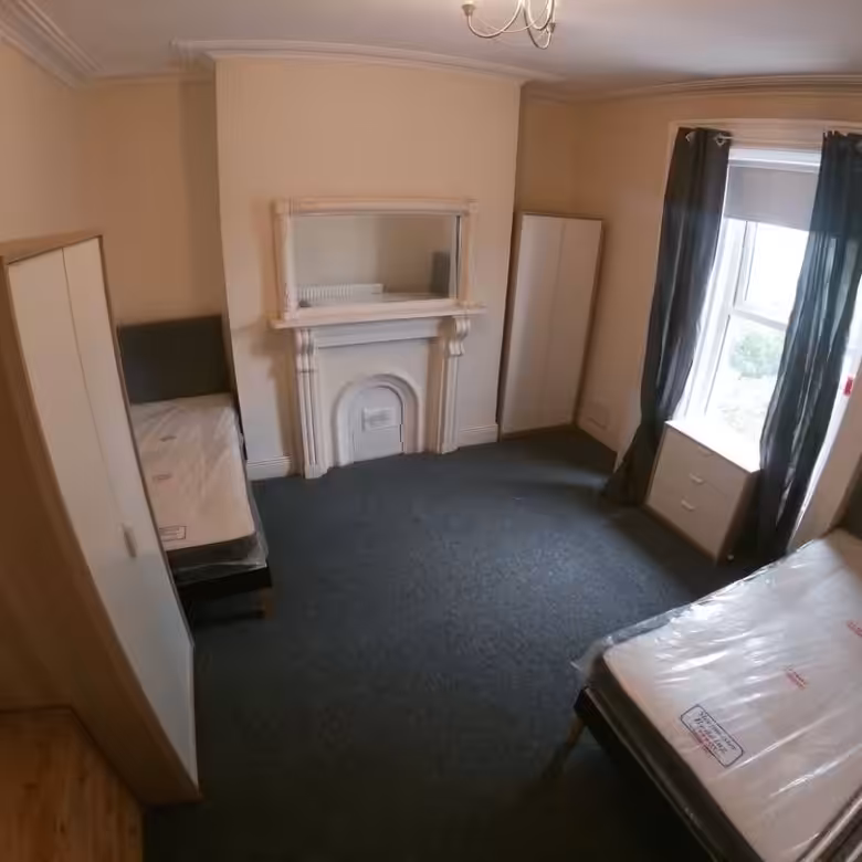 Bedroom with two beds, wardrobes, fireplace, and window with dark curtains.