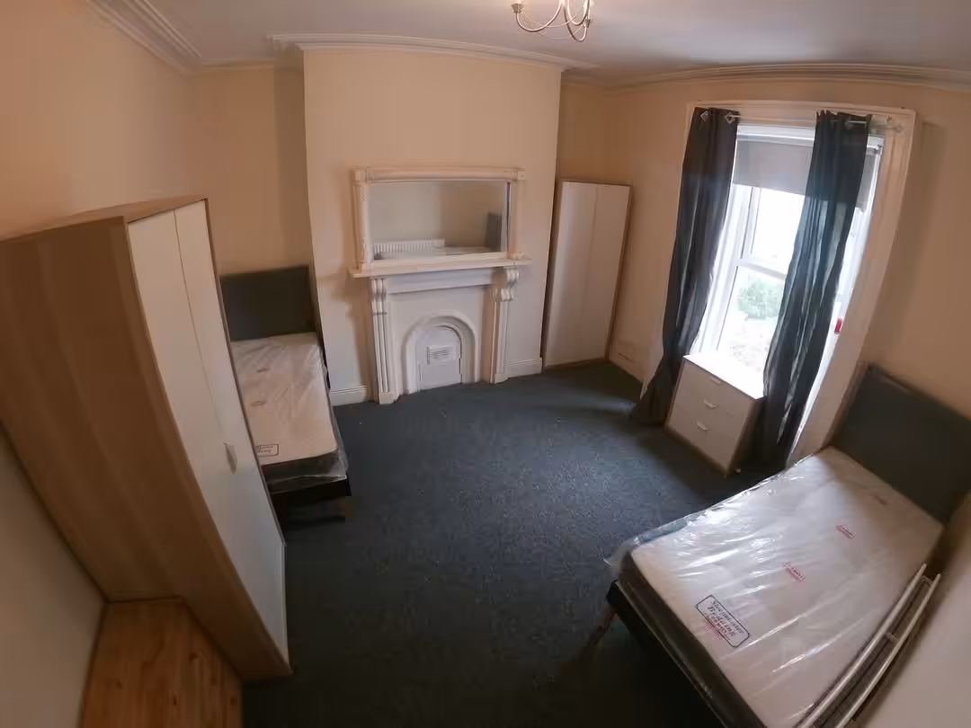 Bedroom with two beds, wardrobes, fireplace, and window with dark curtains.