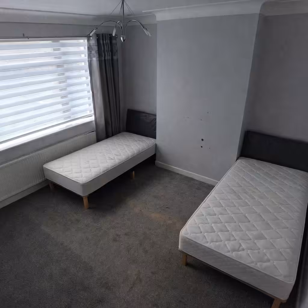 Bedroom with two single beds, window blinds, and gray walls.