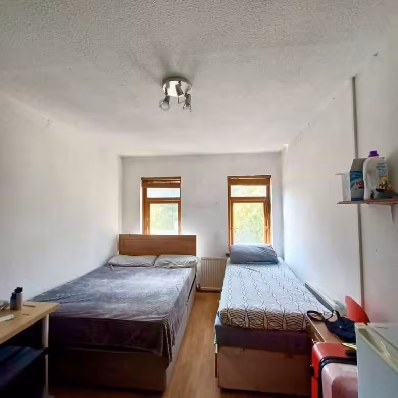 Bedroom with two single beds, small windows, and minimal furniture in a simple, bright interior setting.