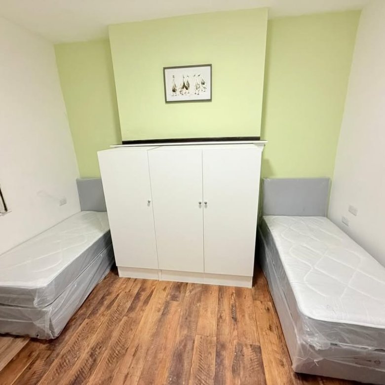 Bedroom with two single beds, wardrobe, wooden floor, and light green accent wall with framed artwork.