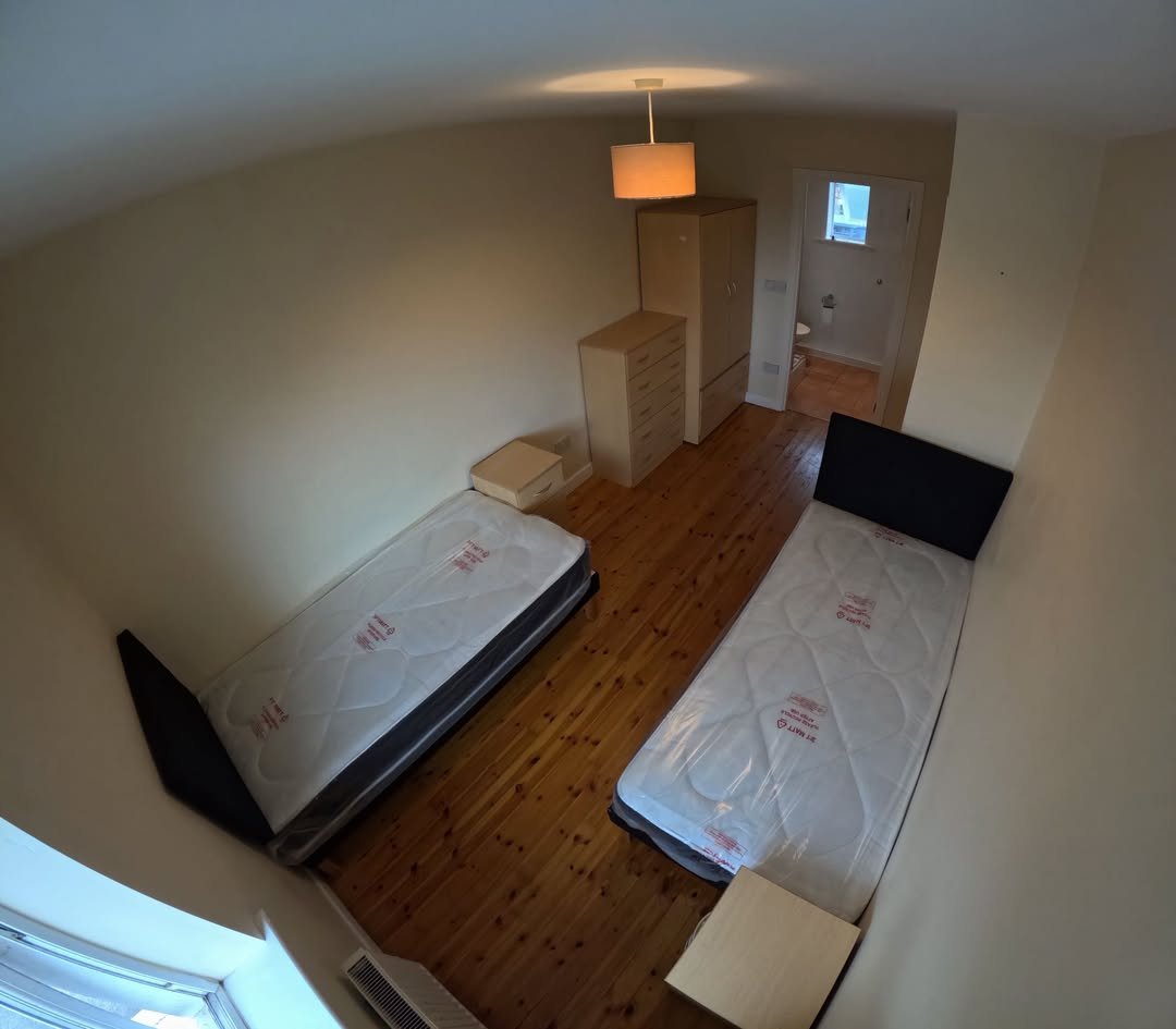 Bedroom with two single beds, wardrobe, and drawers. Neutral tones, wooden floor.