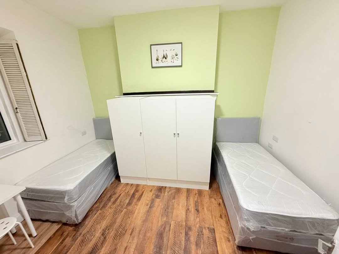 Bedroom with two single beds, wardrobe, wooden floor, and light green accent wall with framed artwork.