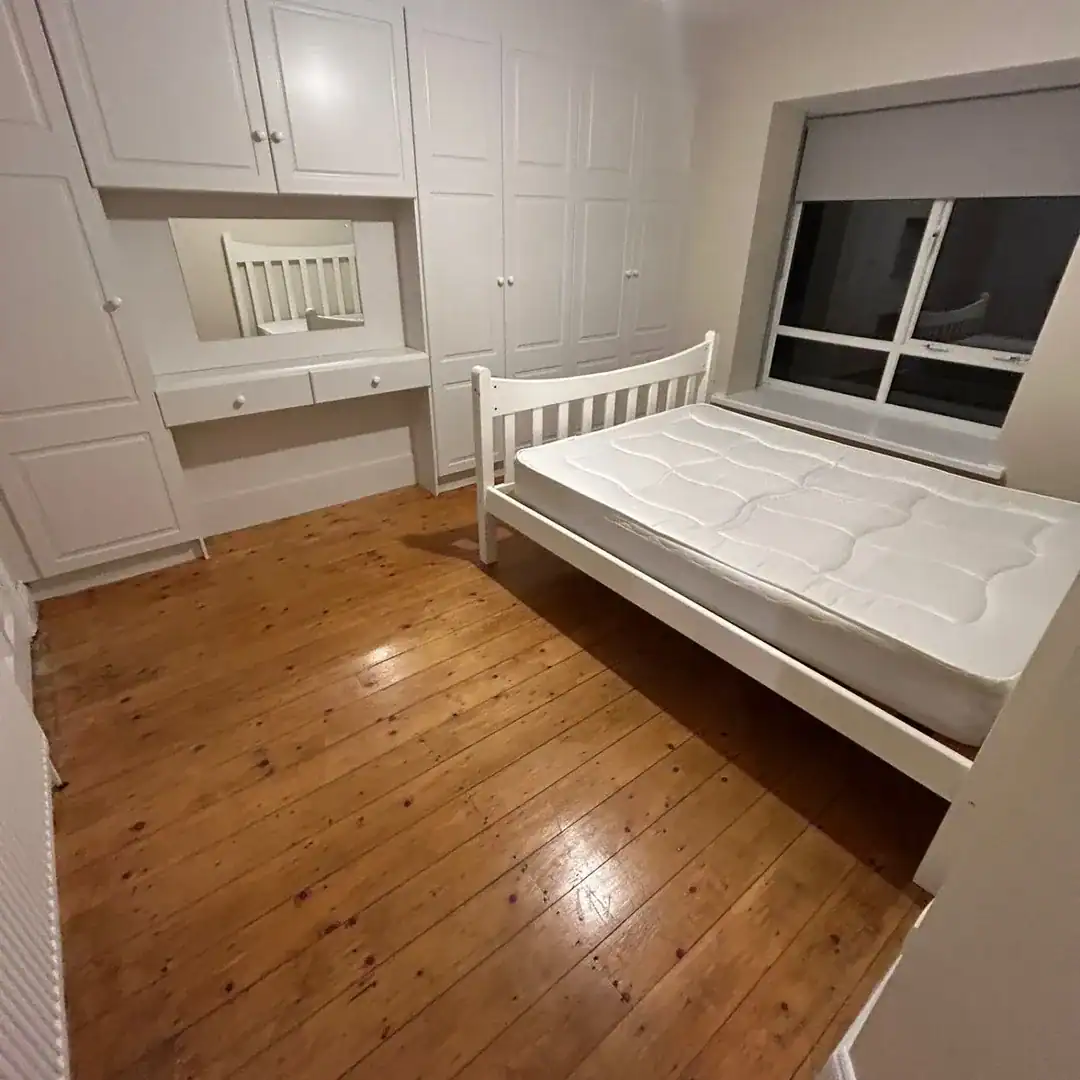 Bedroom interior with white bed, built-in wardrobes, and wooden floor.