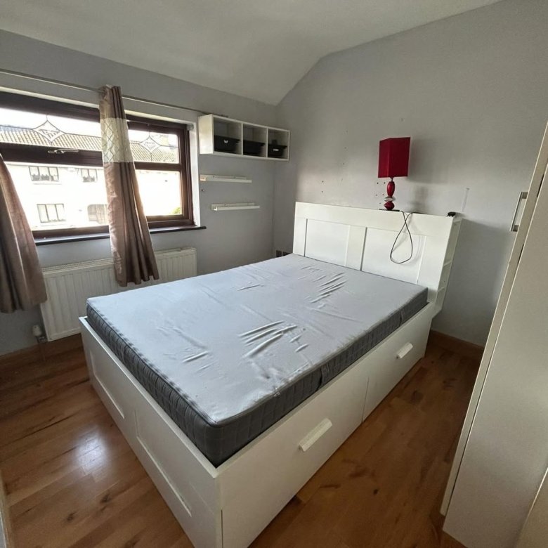 Bedroom with white bed frame, drawers, and gray bedding near window.
