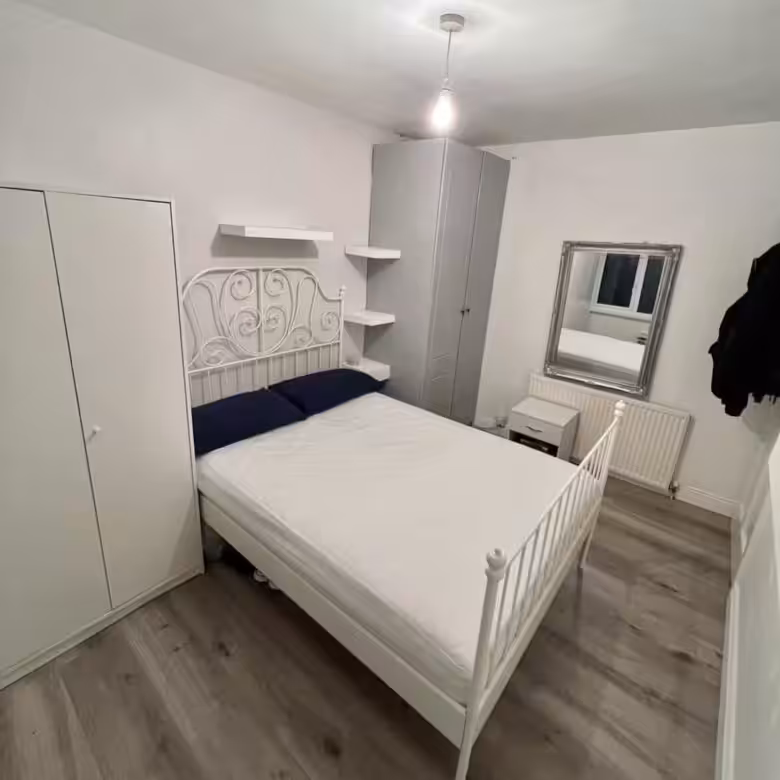 Bedroom with white metal bed, wardrobes, and gray laminate flooring.