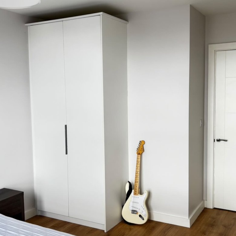 Bedroom corner with white wardrobe, guitar, and white door.