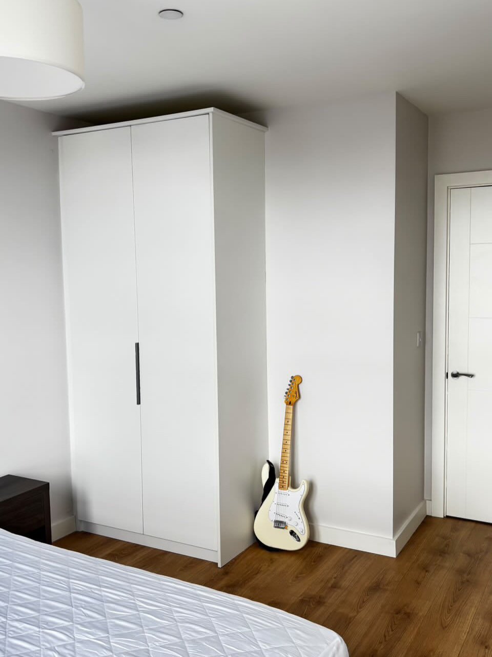 Bedroom corner with white wardrobe, guitar, and white door.