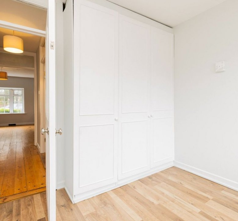 Bedroom with white wardrobe and light wood floors, hallway view.