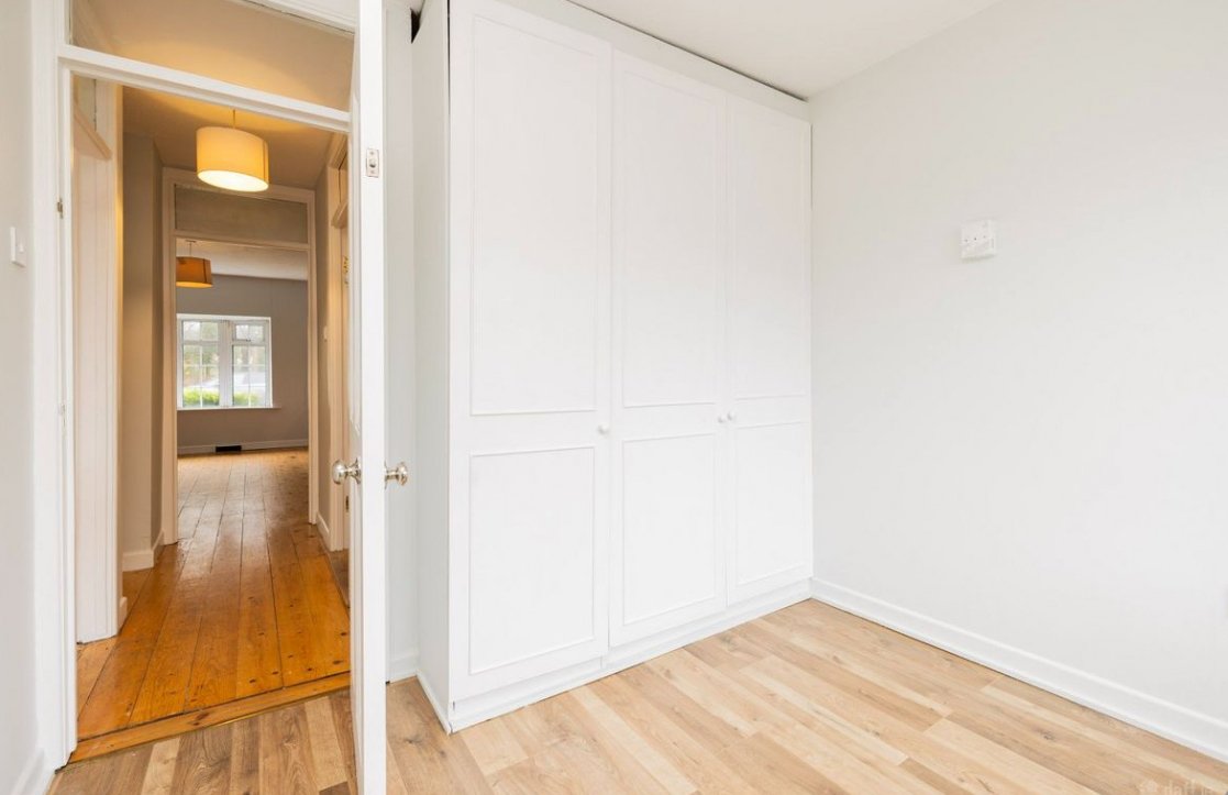 Bedroom with white wardrobe and light wood floors, hallway view.