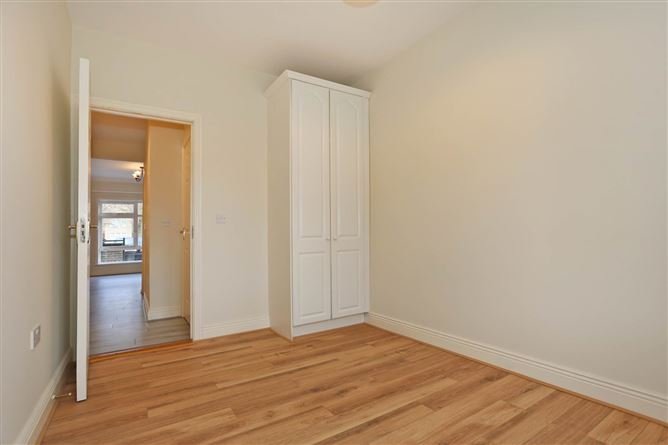 Bedroom with white wardrobe and doorway to another room, wood floors.