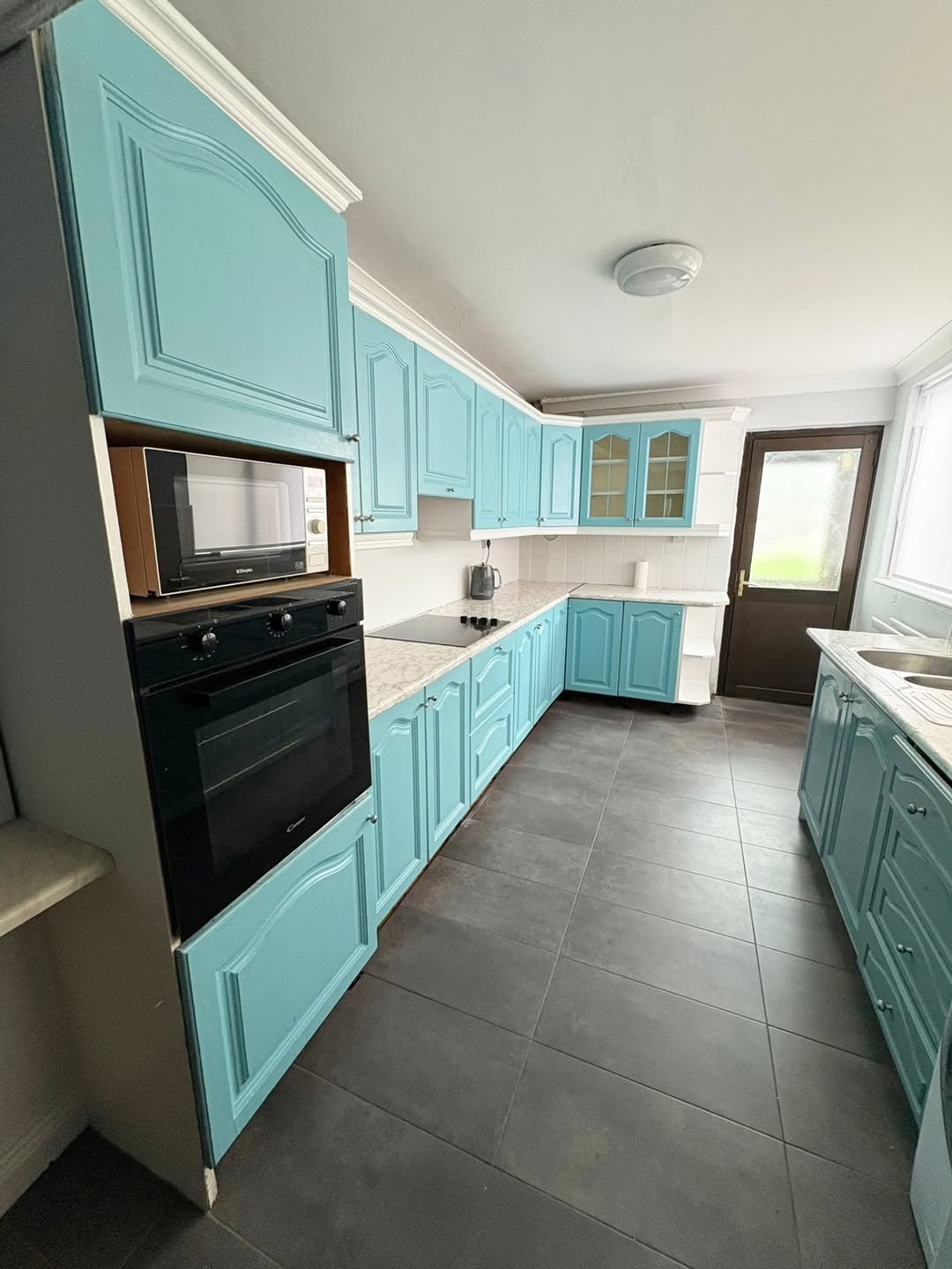 Blue kitchen with black oven and microwave, gray tile floor, white countertops.