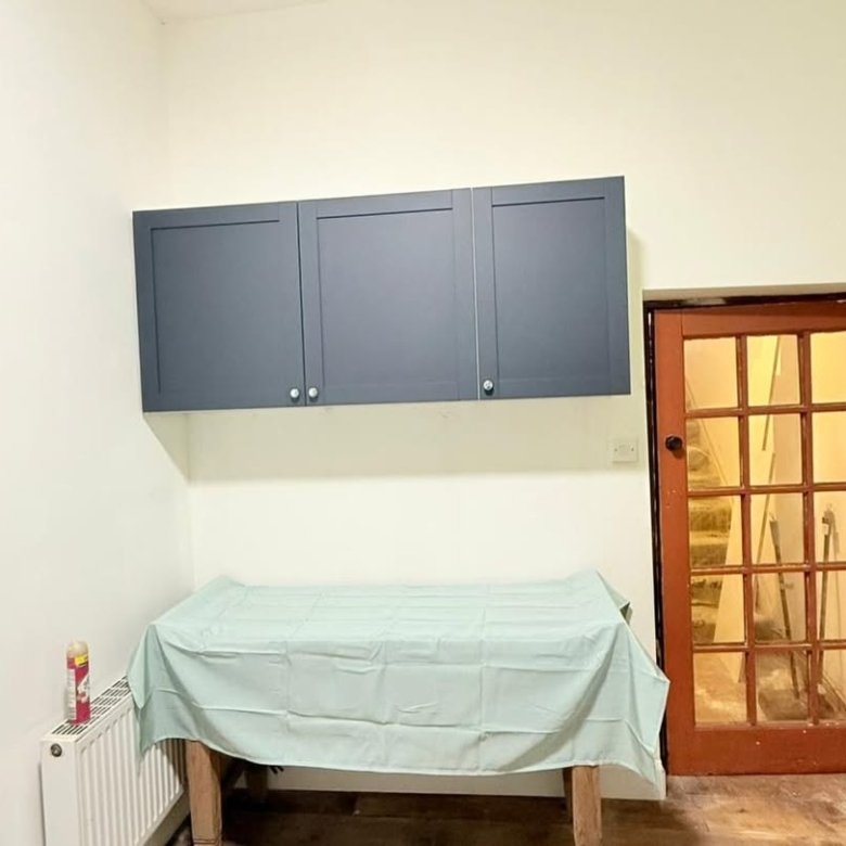 Blue kitchen cabinets above covered table, next to rustic door in room.