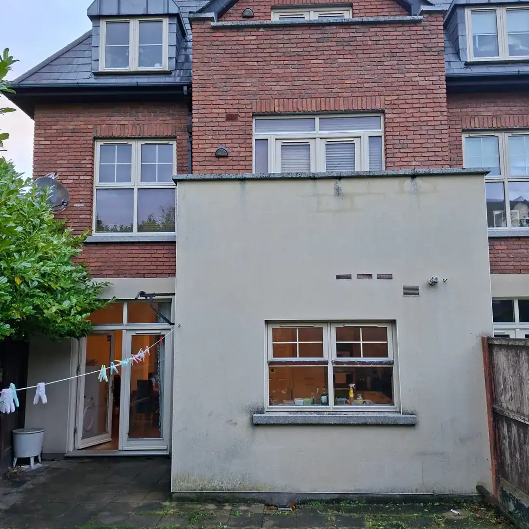 Exterior view of a two-story brick house with a gray extension and clothesline in the backyard.