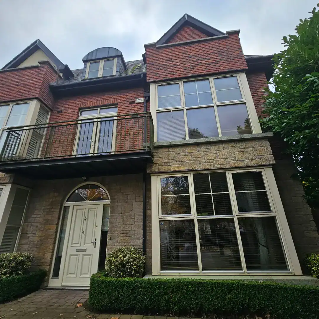 Exterior of brick and stone house with balcony, arched door, and large windows. Neutral color scheme.