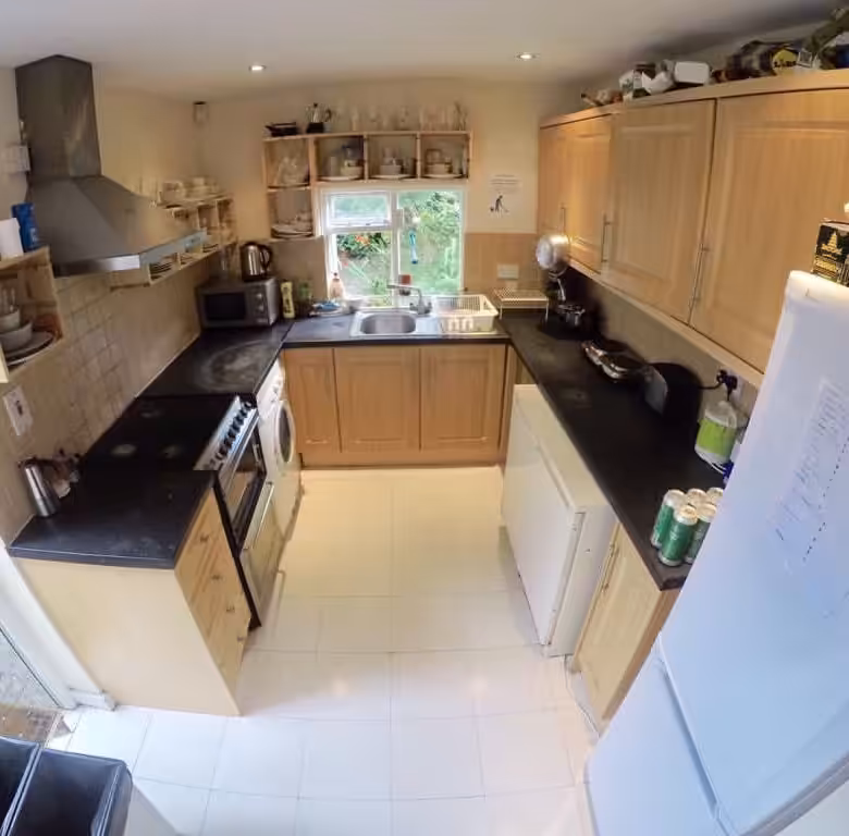 Bright kitchen with light wood cabinets, black countertops, and white tile floor.