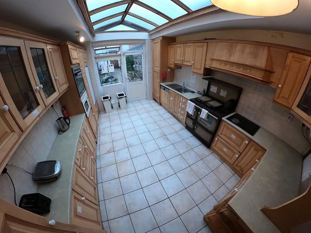 Spacious kitchen with skylight, light wood cabinets, and tile flooring leading to a garden door.