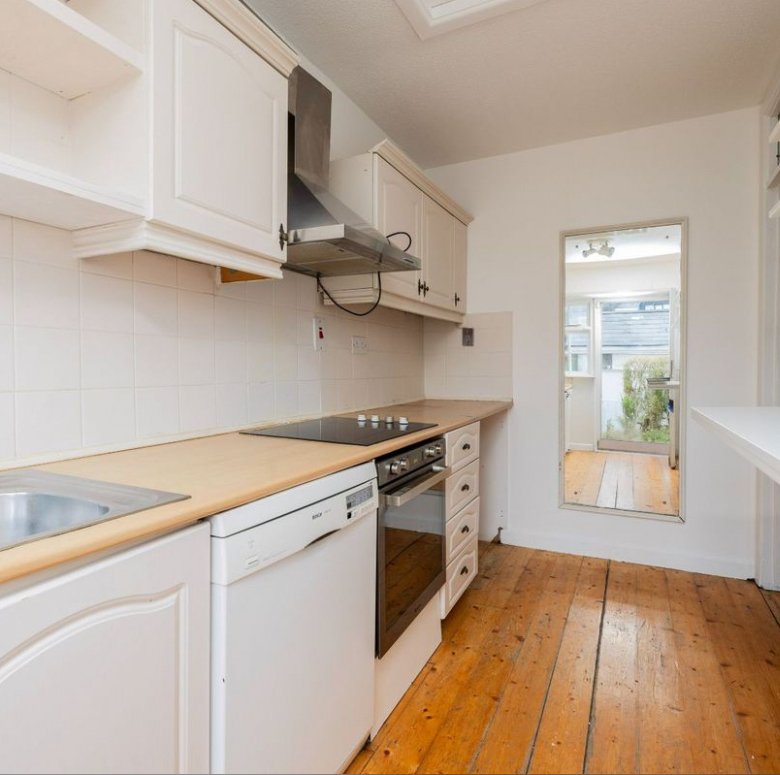 Bright kitchen with white cabinets, wood countertop, and view to garden through doorway.