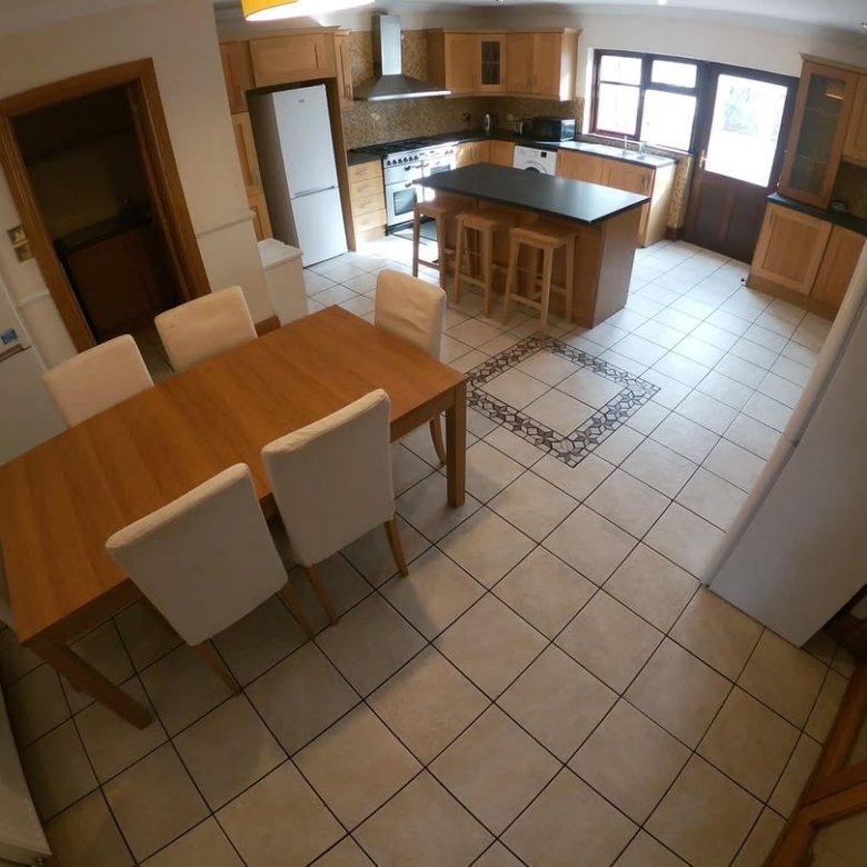 Bright kitchen with wood cabinets, island, dining table, and white appliances. Neutral tile flooring throughout.