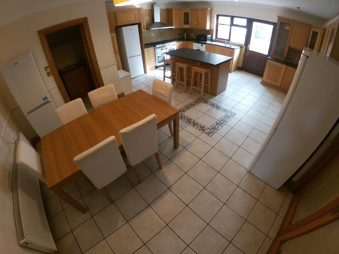 Bright kitchen with wood cabinets, island, dining table, and white appliances. Neutral tile flooring throughout.