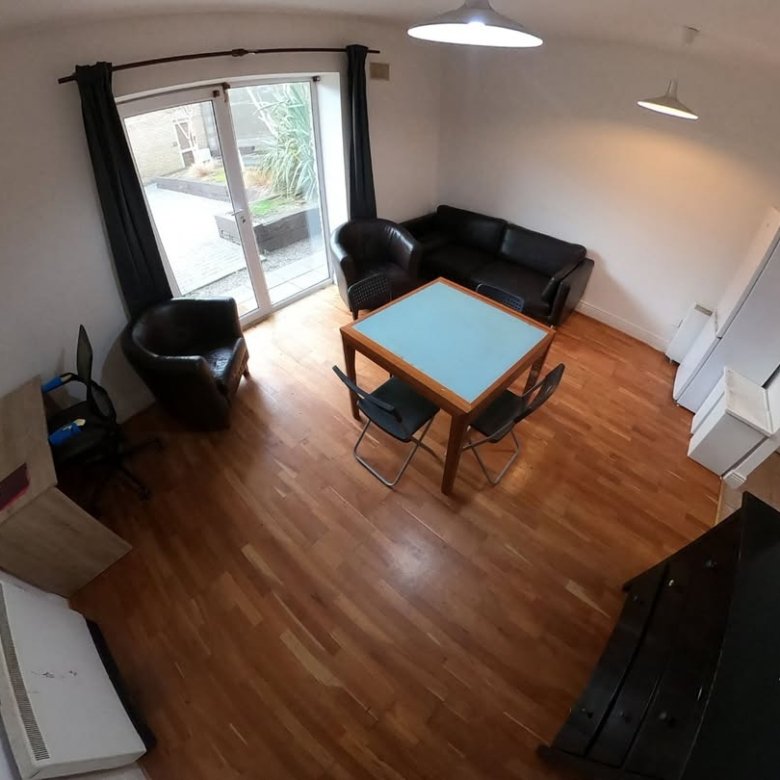 Bright living room with black sofa, chairs, dining table, desk, and natural light from patio door.