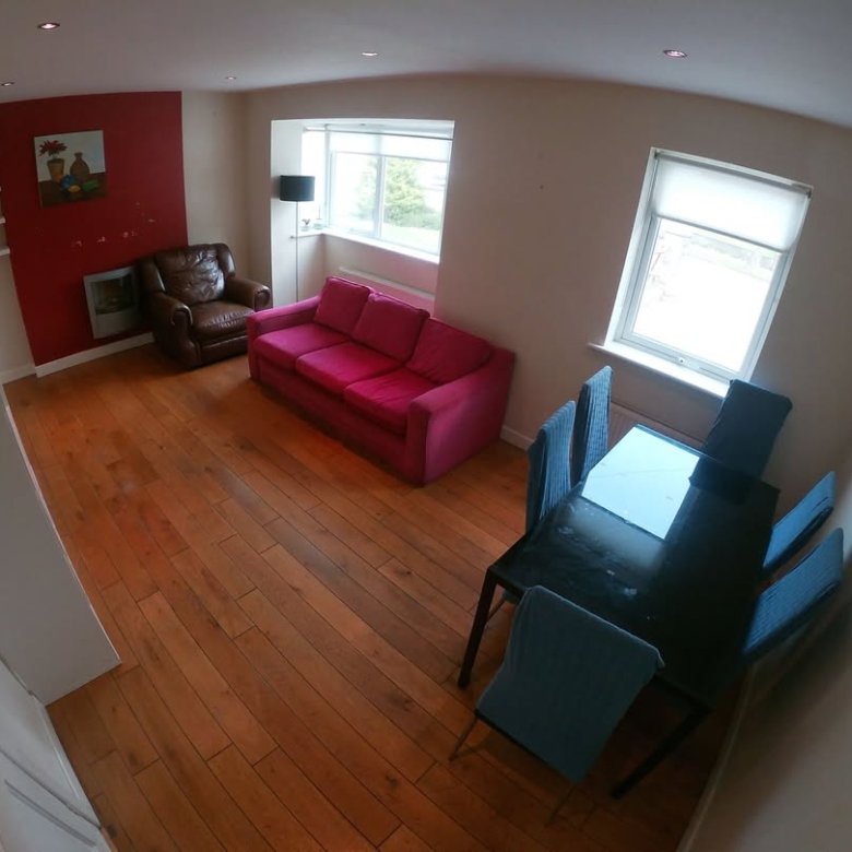 Living room with pink sofa, dining table, and red accent wall. Bright interior.