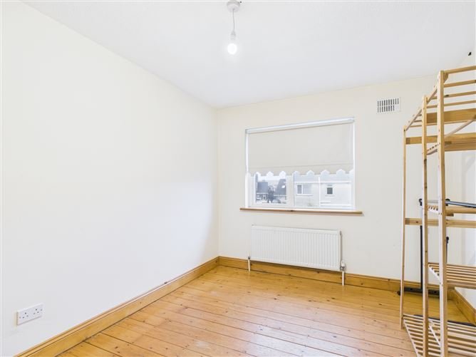 Bright room with wooden floor, white walls, window with blind, radiator, and wooden shelving unit.