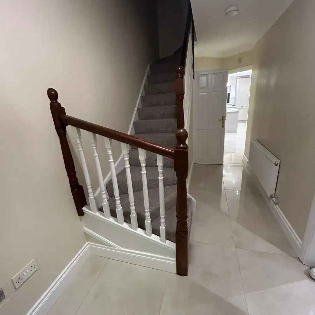 Hallway with carpeted stairs, white spindles, and dark wood banister leading to an open doorway.