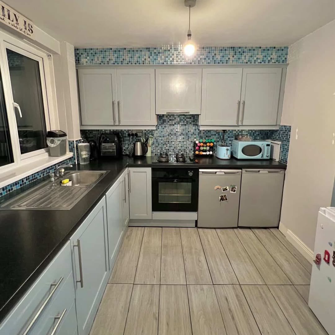 Compact kitchen with gray cabinets, black countertop, and blue mosaic backsplash.