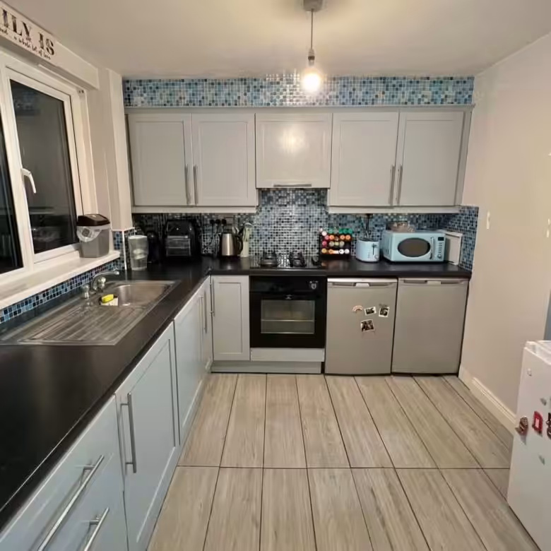 Compact kitchen with gray cabinets, blue mosaic backsplash, and wood-look tile flooring.