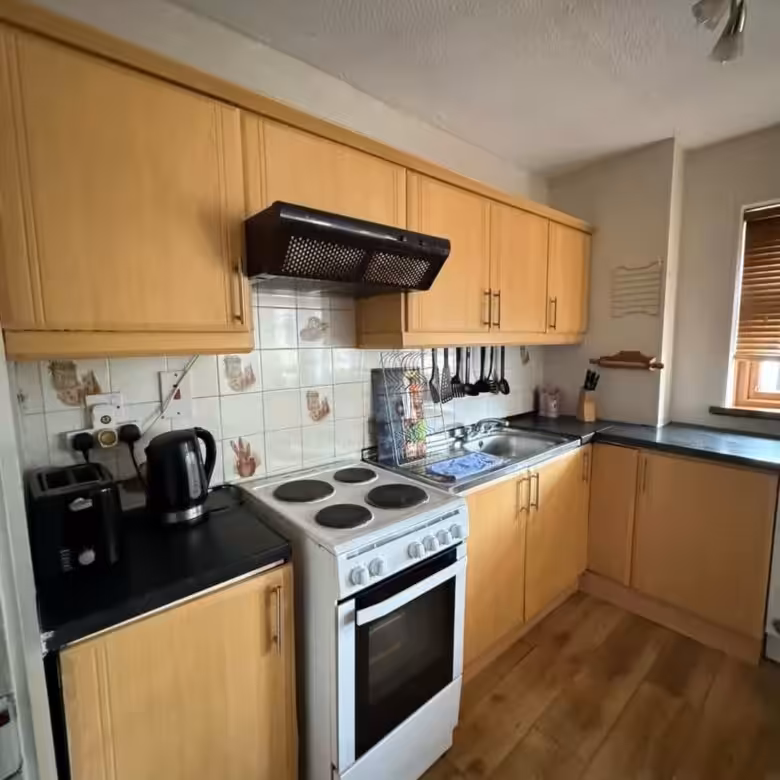 Compact kitchen with light wood cabinets, white stove, and black countertops.