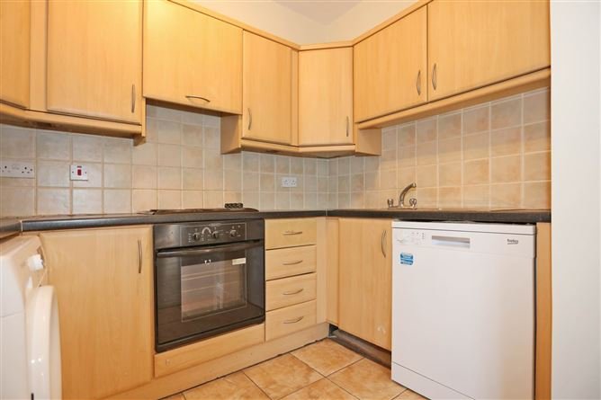 Compact kitchen with light wood cabinets, tile backsplash, black countertops, oven, and white dishwasher.