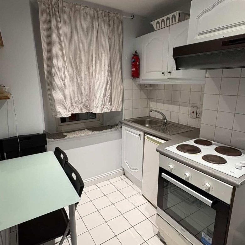 Compact kitchen with white cabinets, oven, and dining table near a window.