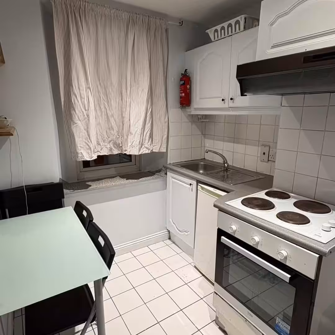 Compact kitchen with white cabinets, oven, and dining table near a window.