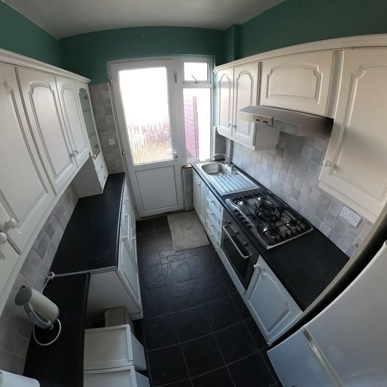 Compact kitchen with white cabinets, dark countertops, and teal walls. Gas stove and tile backsplash visible.