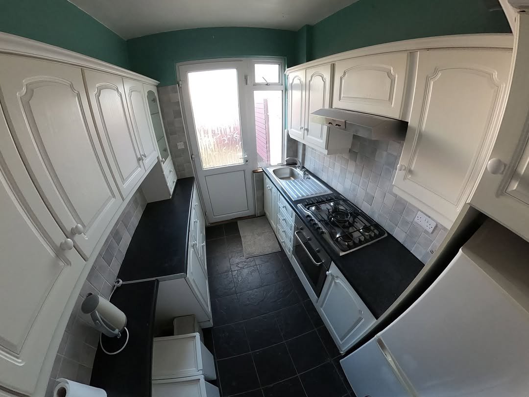 Compact kitchen with white cabinets, dark countertops, and teal walls. Gas stove and tile backsplash visible.