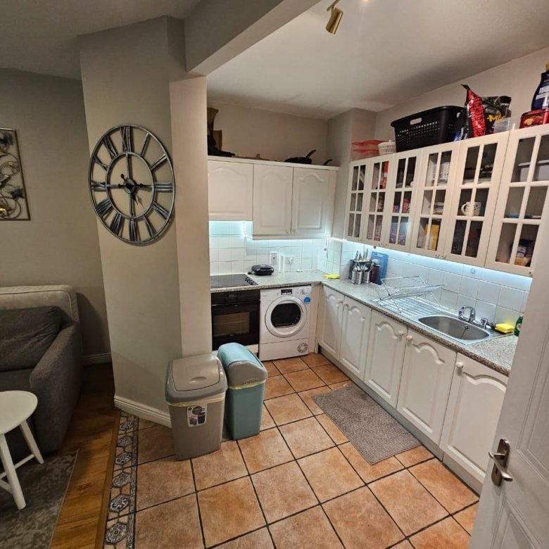 Compact kitchen with white cabinets, appliances, tile floor, and large clock on wall.