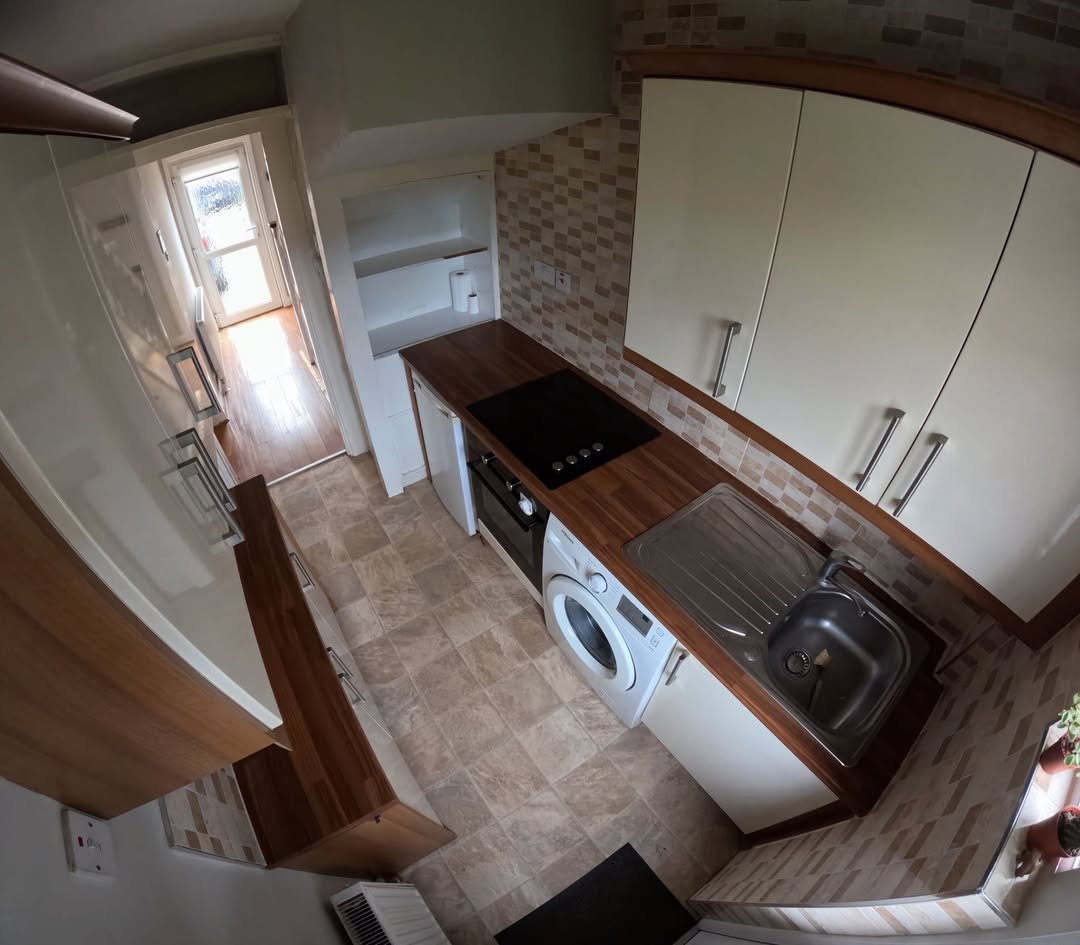 Compact kitchen with white cabinets, wood countertops, and a washing machine.