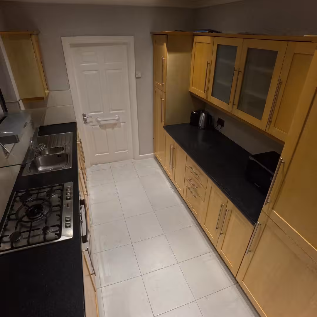 Compact kitchen with light wood cabinets, black countertops, and gas hob.