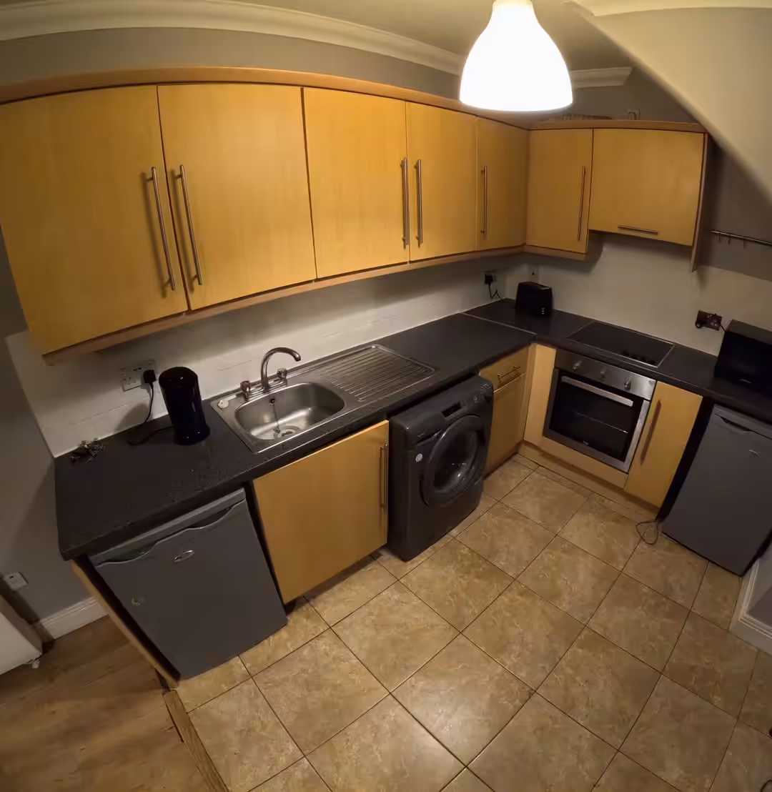 Compact kitchen with light wood cabinets, black countertop, and tile flooring.