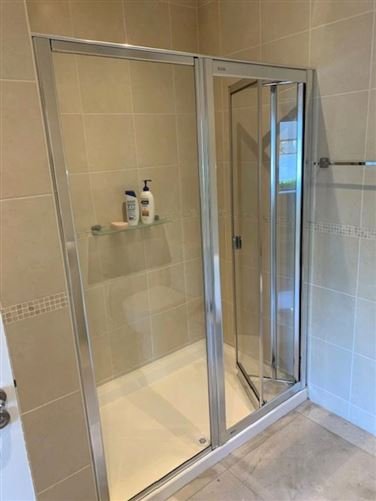Corner shower with folding glass door and beige tiled walls.