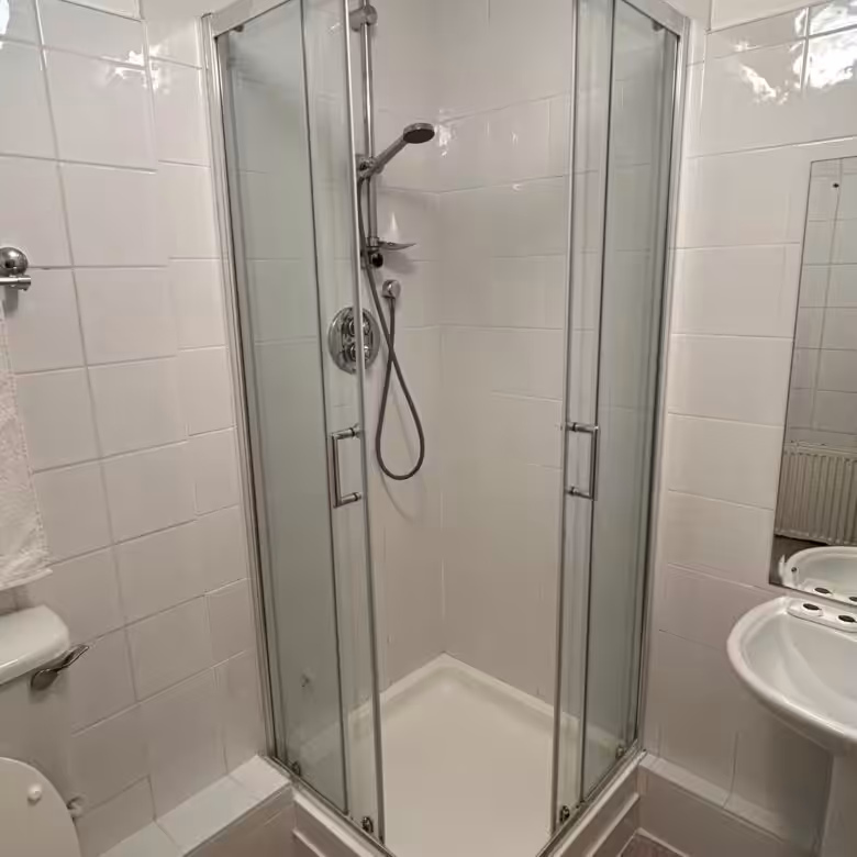 Corner shower stall with glass doors in a tiled bathroom.