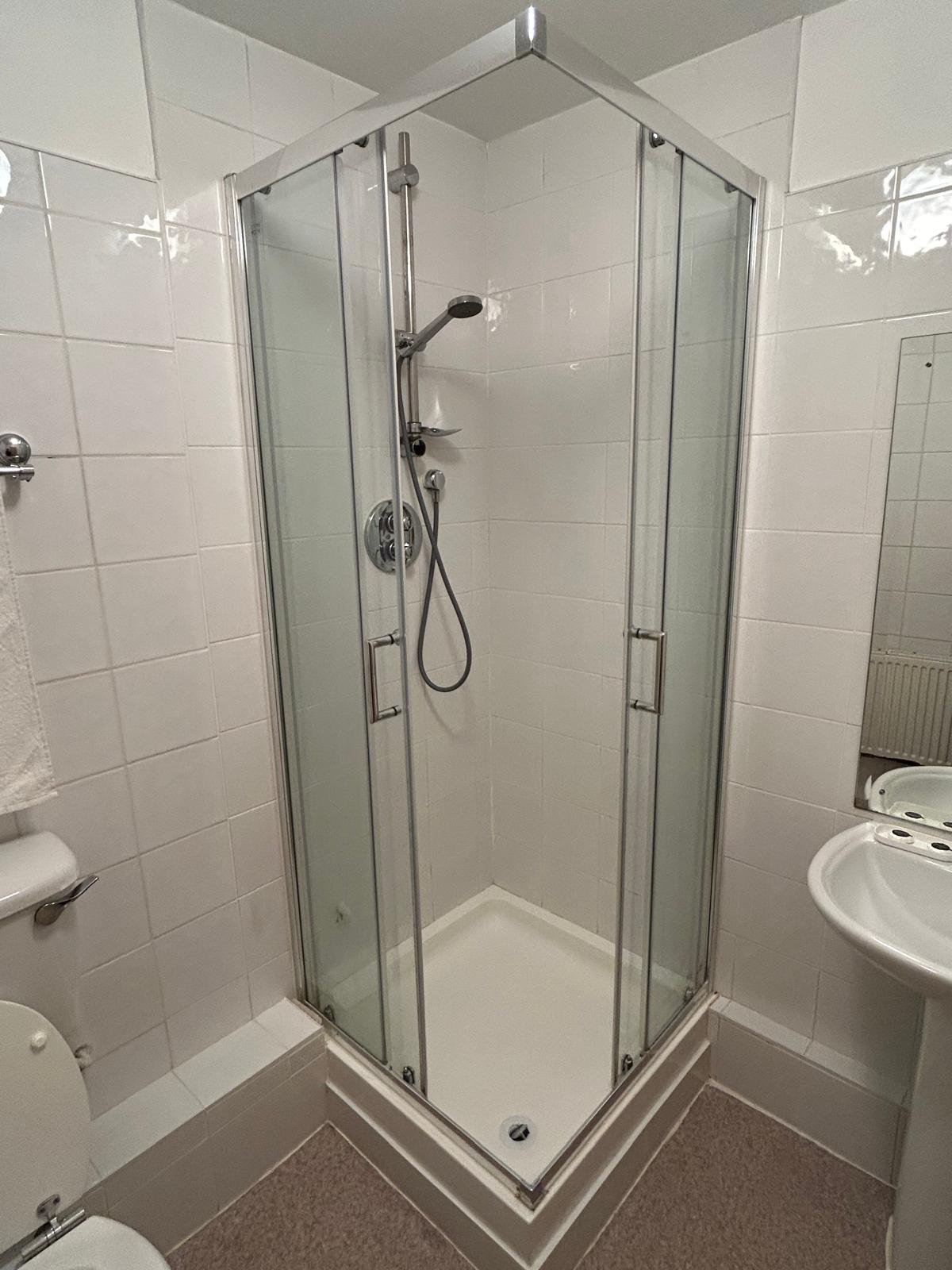Corner shower stall with glass doors in a tiled bathroom.