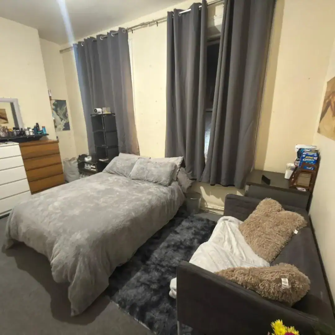Cozy bedroom with gray bedding, curtains, and rug, featuring a bed, futon, and storage shelves.