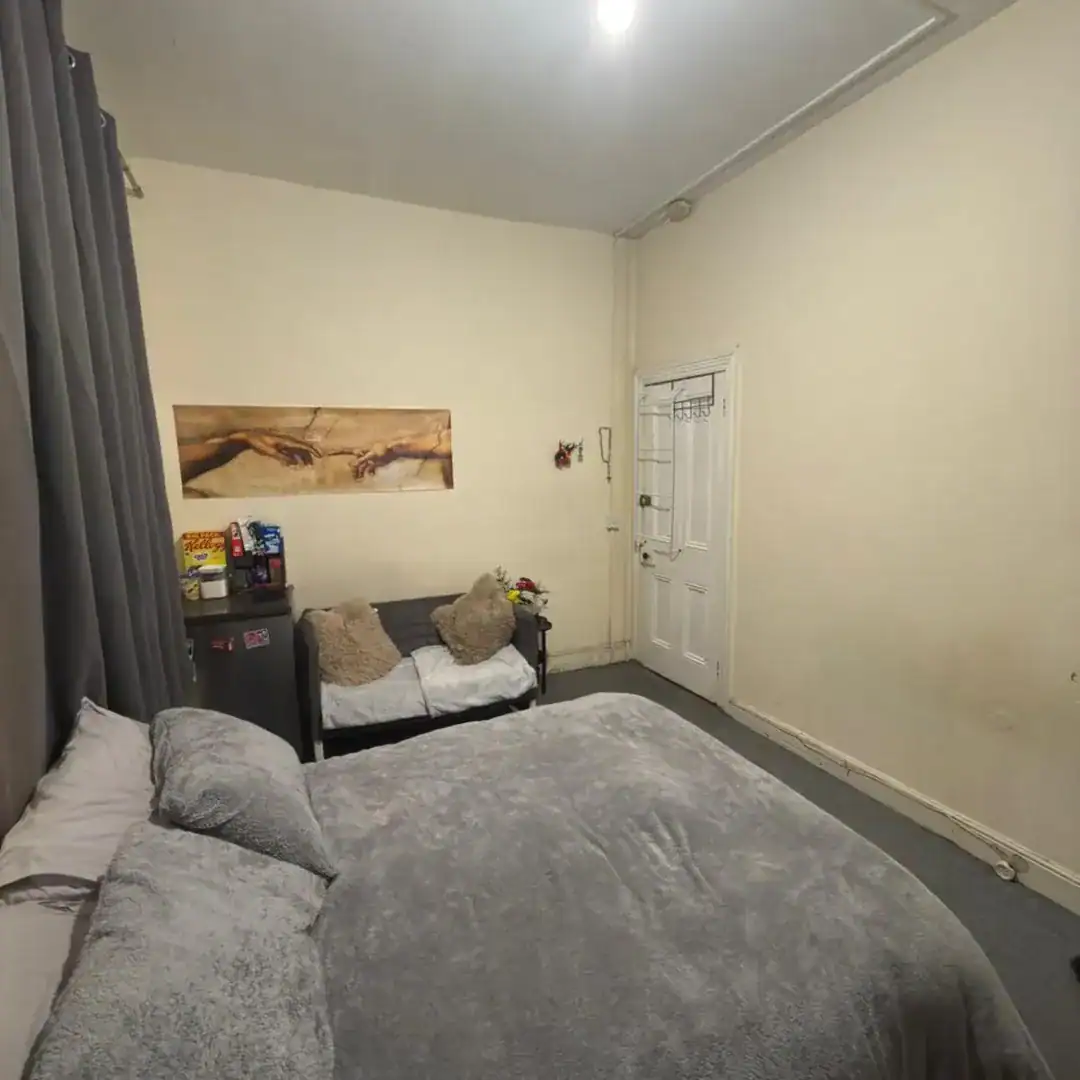 Cozy room with bed, sofa, mini fridge, and art print of Michelangelo's Creation of Adam on the wall.